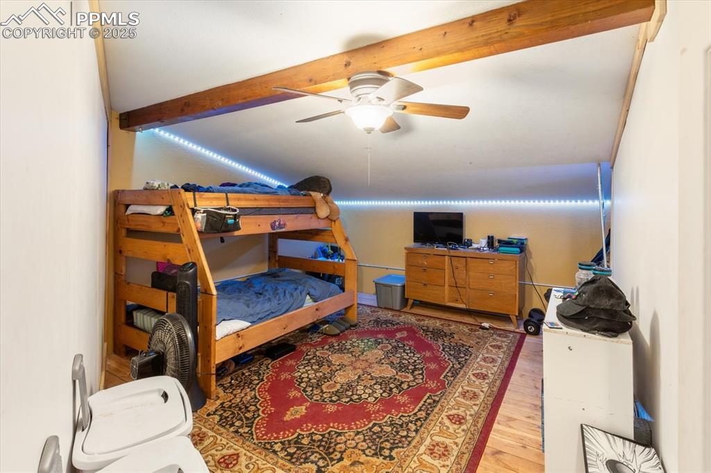 Image 27 of 45: Bedroom with beamed ceiling, wood finished floors, and ceiling fan