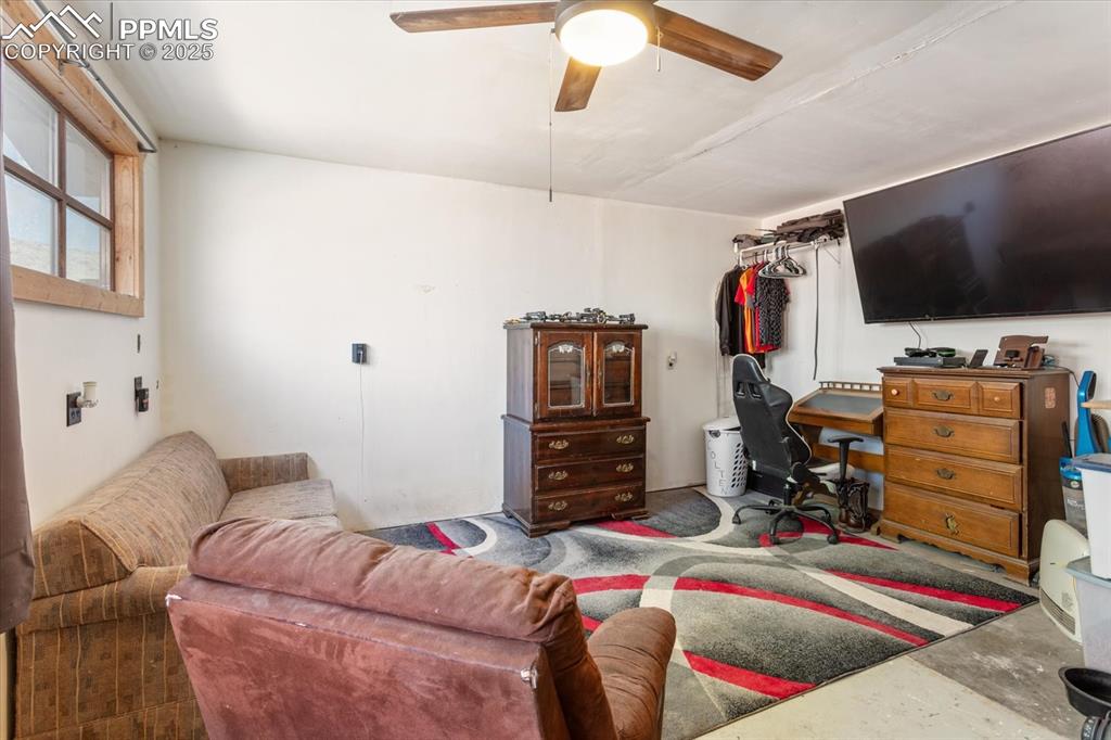 Image 34 of 45: Living room with a ceiling fan and concrete flooring