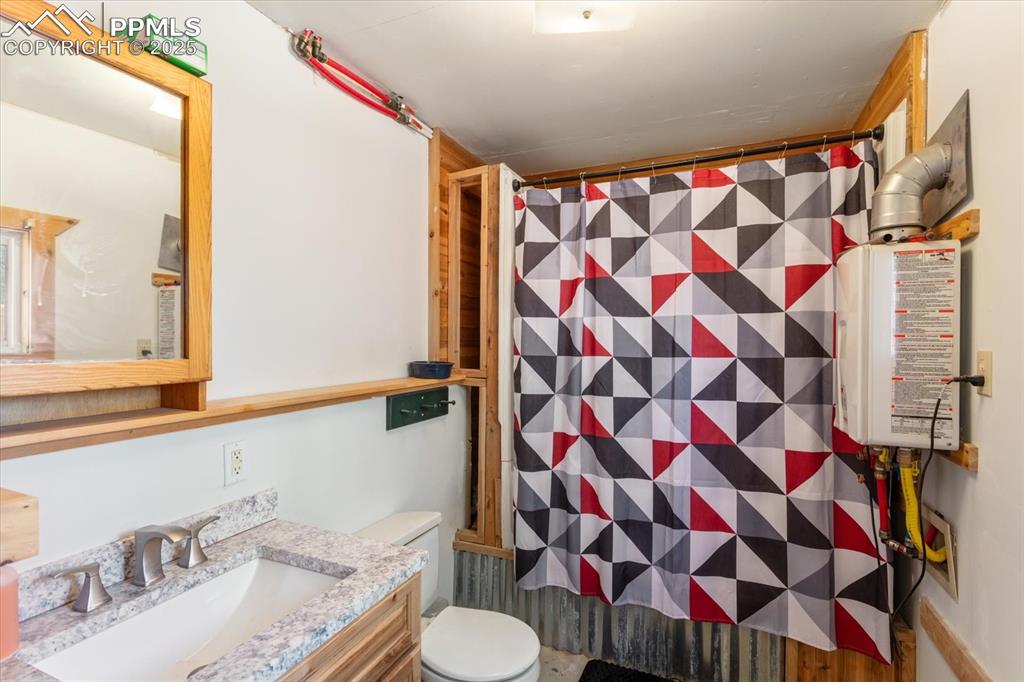 Image 36 of 45: Bathroom featuring toilet, vanity, curtained shower, and tankless water hea