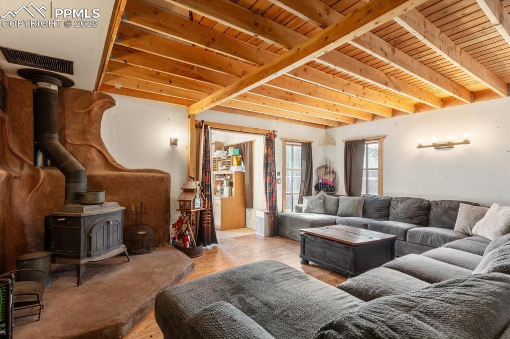 Image 8 of 45: Living area with a wood stove, wooden ceiling with exposed beams, and wood 