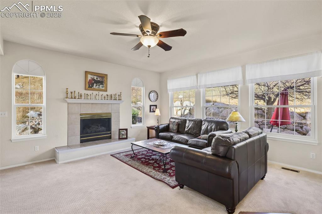 Image 14 of 49: Carpeted living room featuring a tile fireplace, a ceiling fan, and plenty 