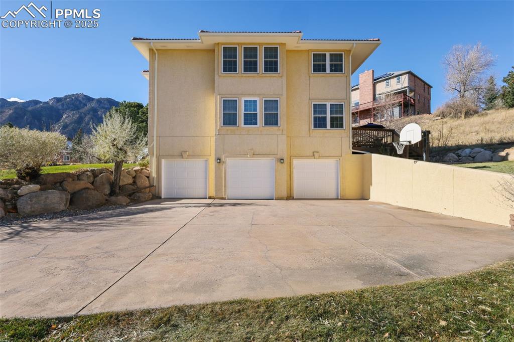 Image 38 of 49: Back of house featuring concrete driveway, stucco siding, a garage, a mount