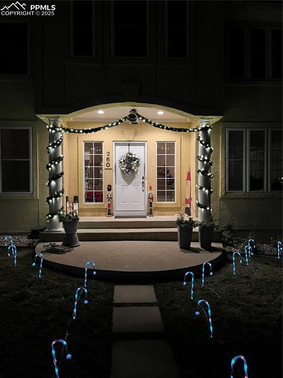 Image 43 of 49: Exterior entry at night featuring stucco siding