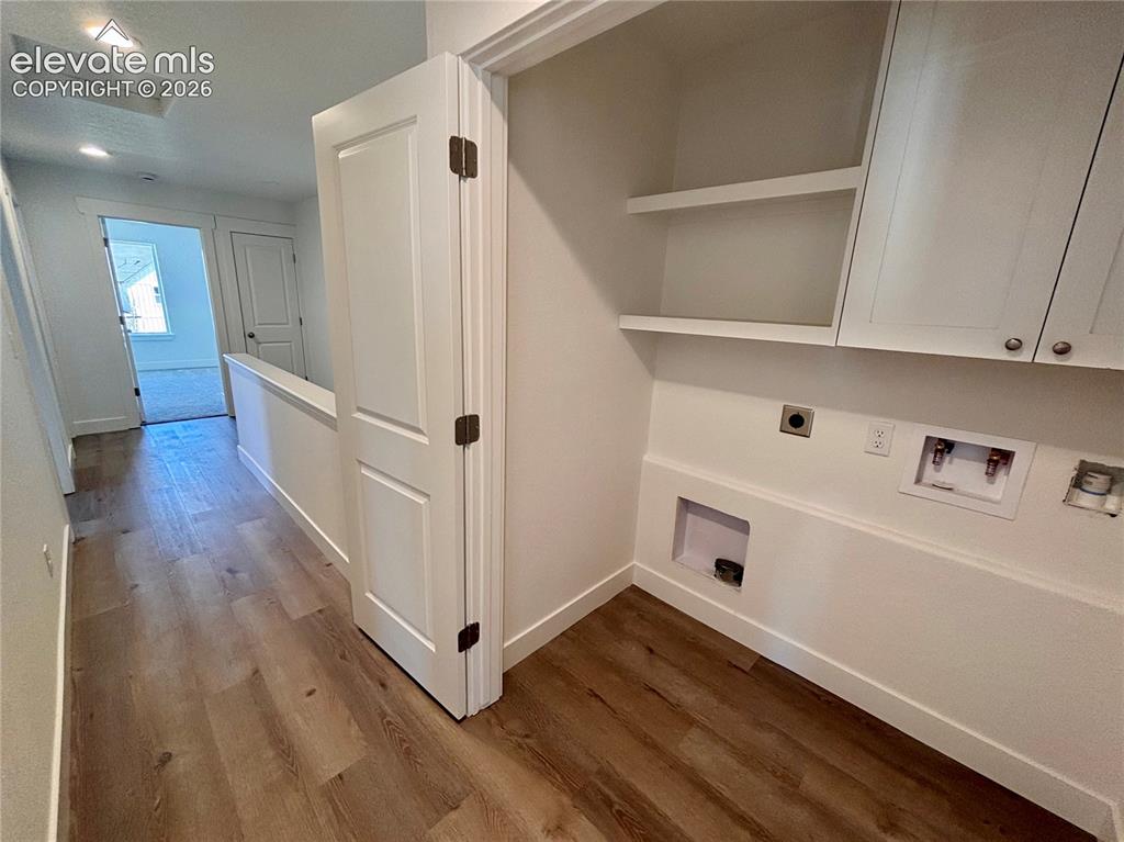 Image 21 of 23: Laundry area featuring upper cabinetry, shelving, and wood-finish flooring