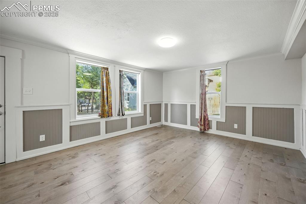 Image 11 of 25: Unfurnished room with crown molding, light wood-style flooring, wainscoting