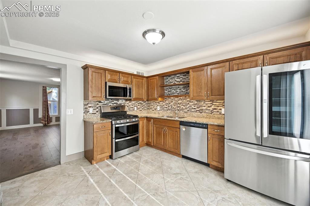 Image 13 of 25: Kitchen with stainless steel appliances, light stone counters, brown cabine