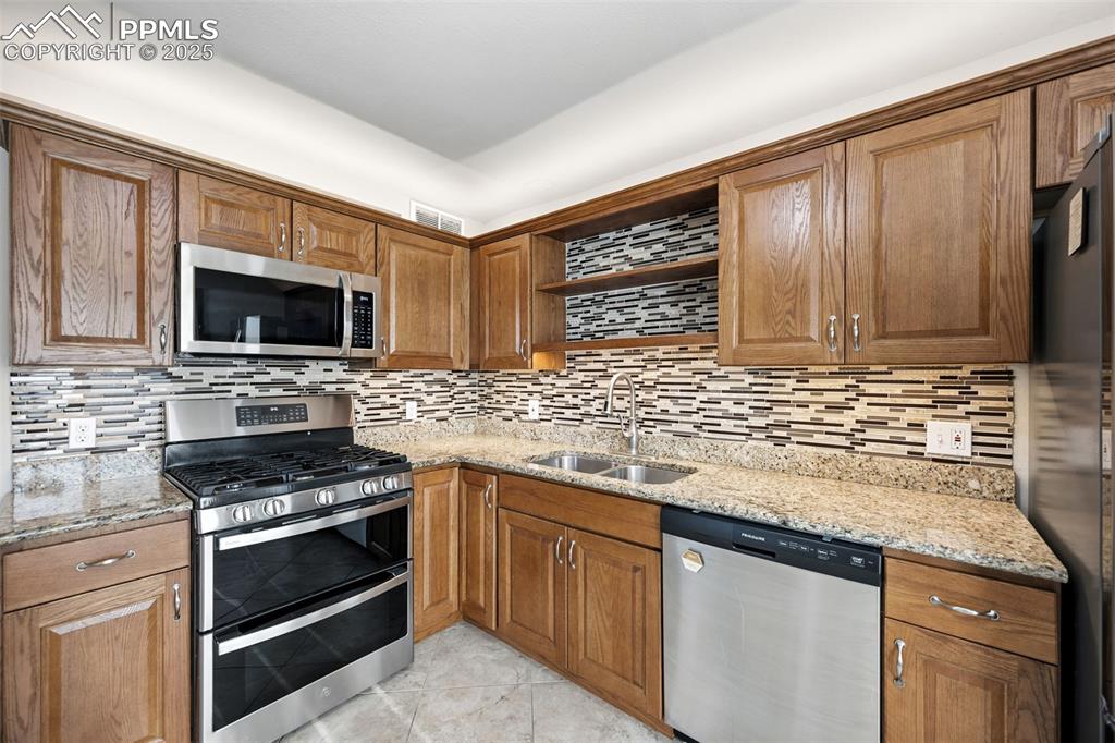 Image 14 of 25: Kitchen with appliances with stainless steel finishes, light stone countert