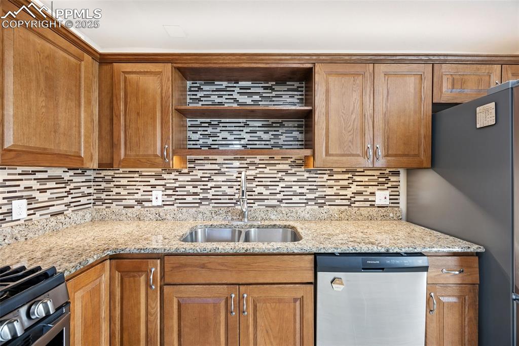 Image 16 of 25: Kitchen featuring appliances with stainless steel finishes, light stone cou