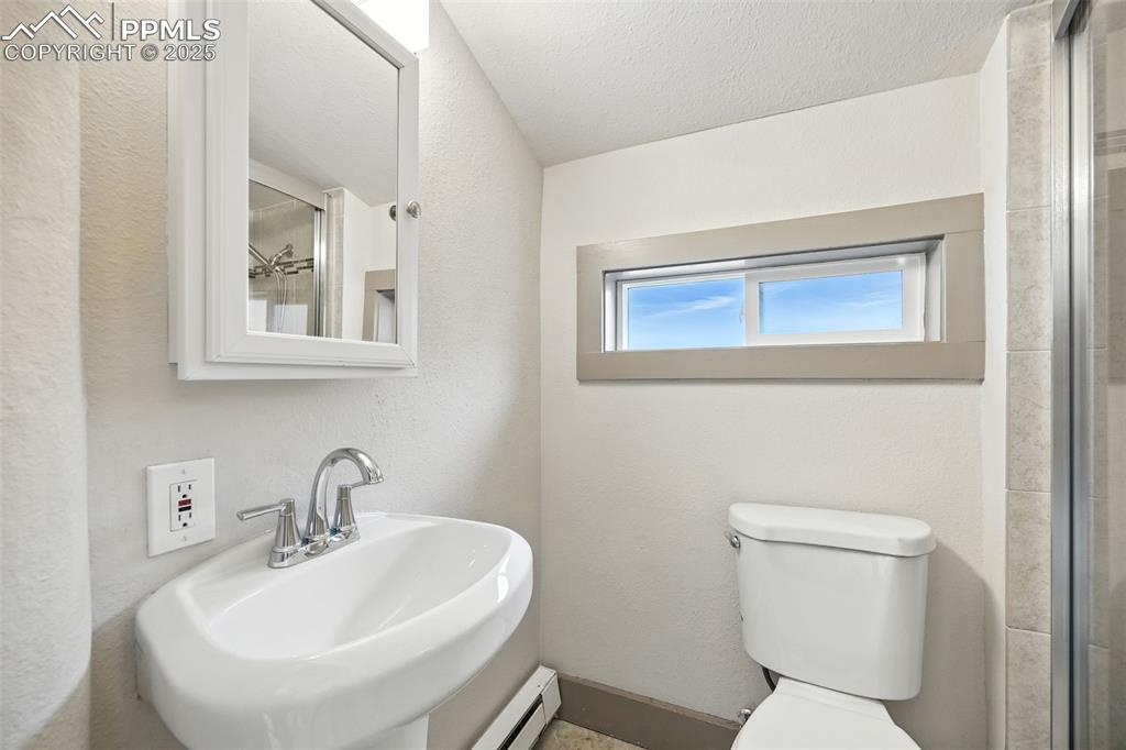 Image 18 of 25: Full bathroom featuring a textured wall, a baseboard radiator, a tile showe