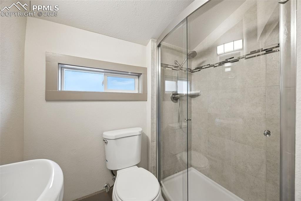 Image 19 of 25: Bathroom featuring a shower stall, lofted ceiling, and a textured ceiling