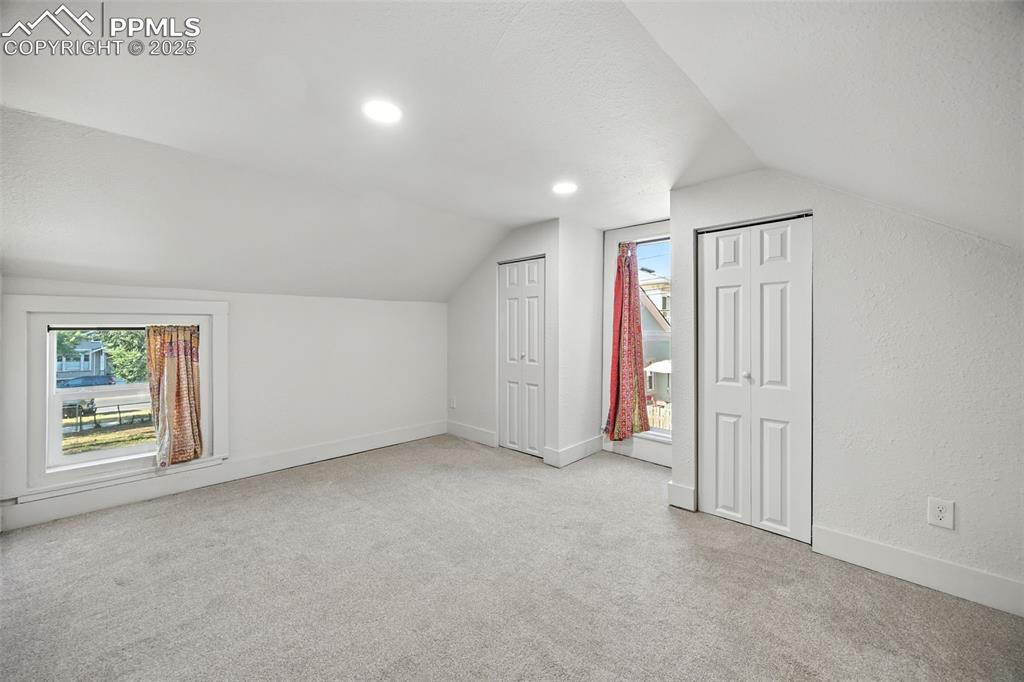 Image 23 of 25: Additional living space featuring light carpet, lofted ceiling, a textured 