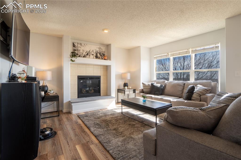 Image 12 of 40: Living area featuring a tiled fireplace, wood finished floors, and a textur