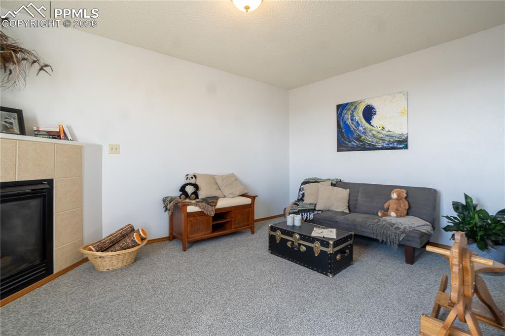 Image 18 of 40: Living area with a tiled fireplace, carpet, and a textured ceiling