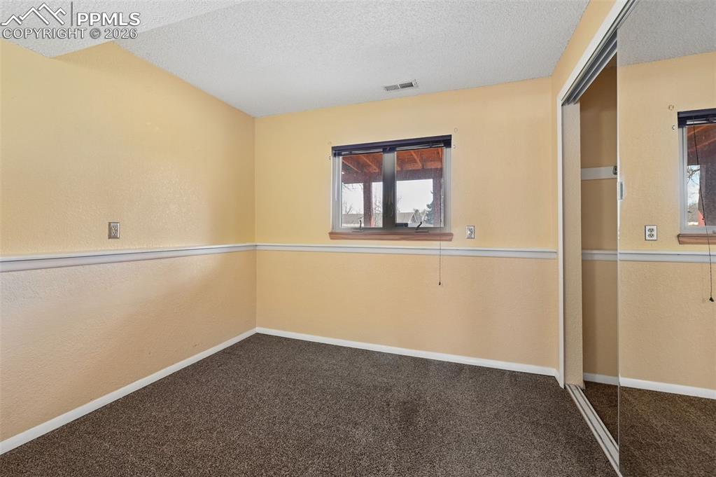 Image 19 of 25: Empty room with a textured wall, dark carpet, and a textured ceiling
