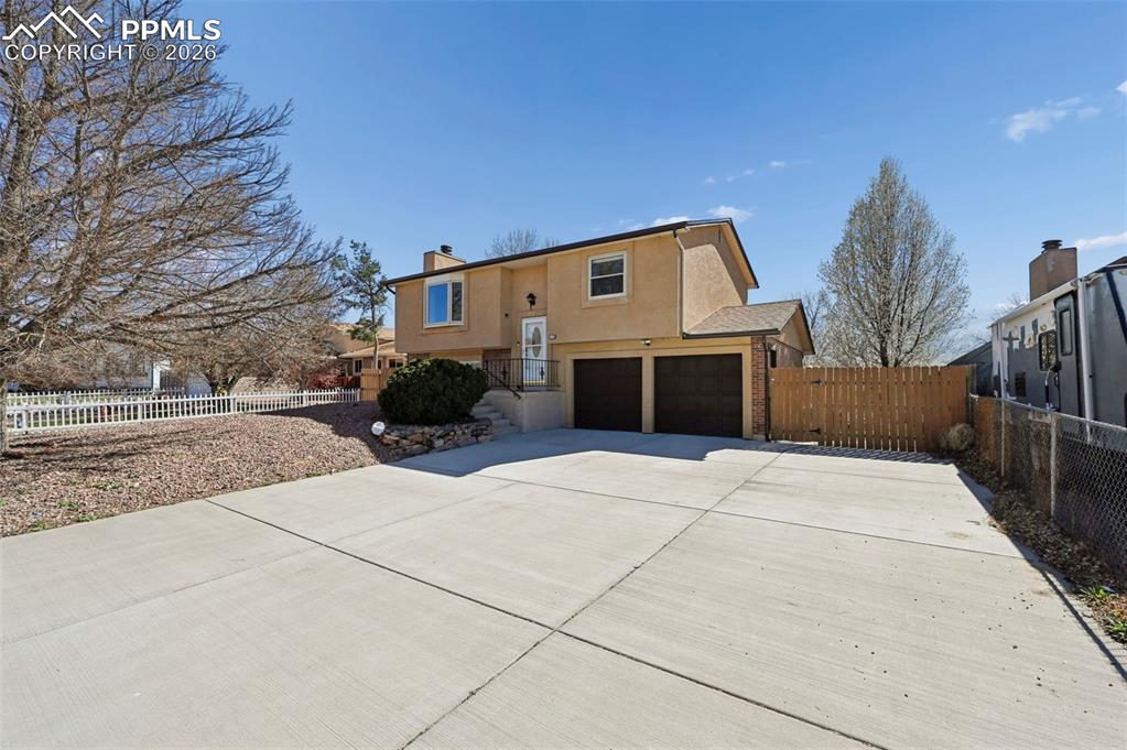 Image 2 of 25: View of front of property with stucco siding, a garage, driveway, a chimney
