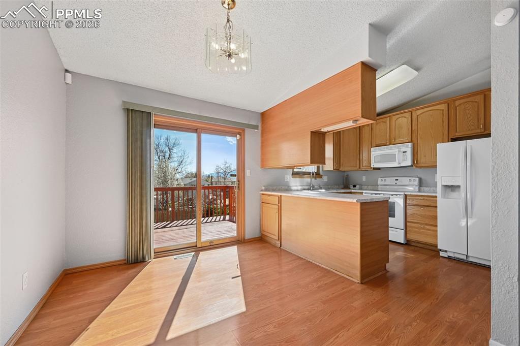 Image 7 of 25: Kitchen with light countertops, a peninsula, white appliances, suspended li