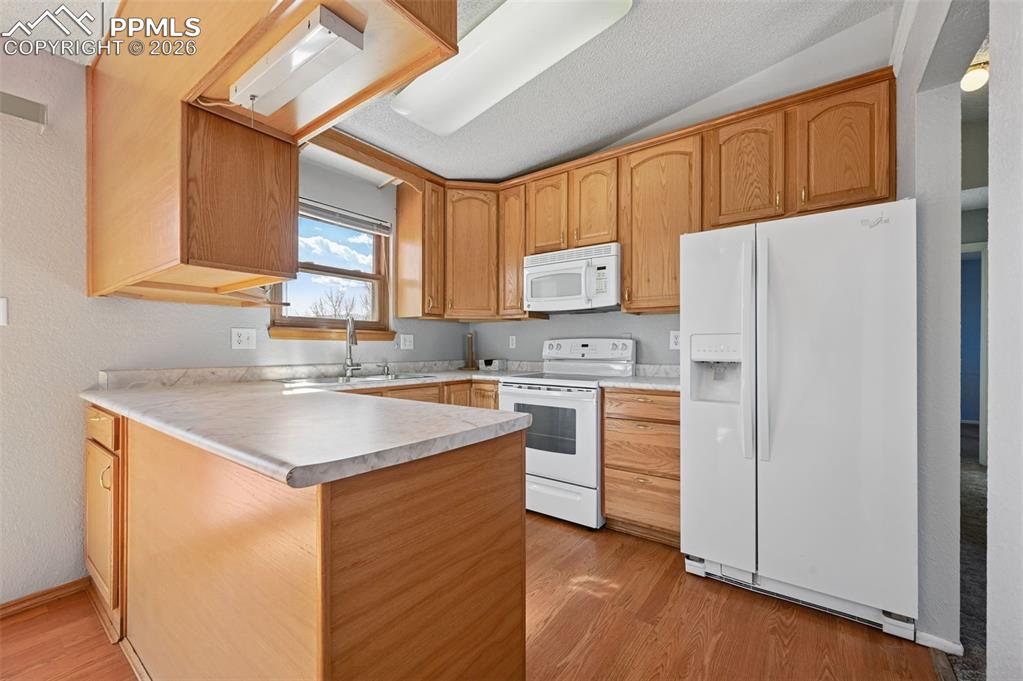Image 8 of 25: Kitchen with white appliances, light countertops, a peninsula, a textured w