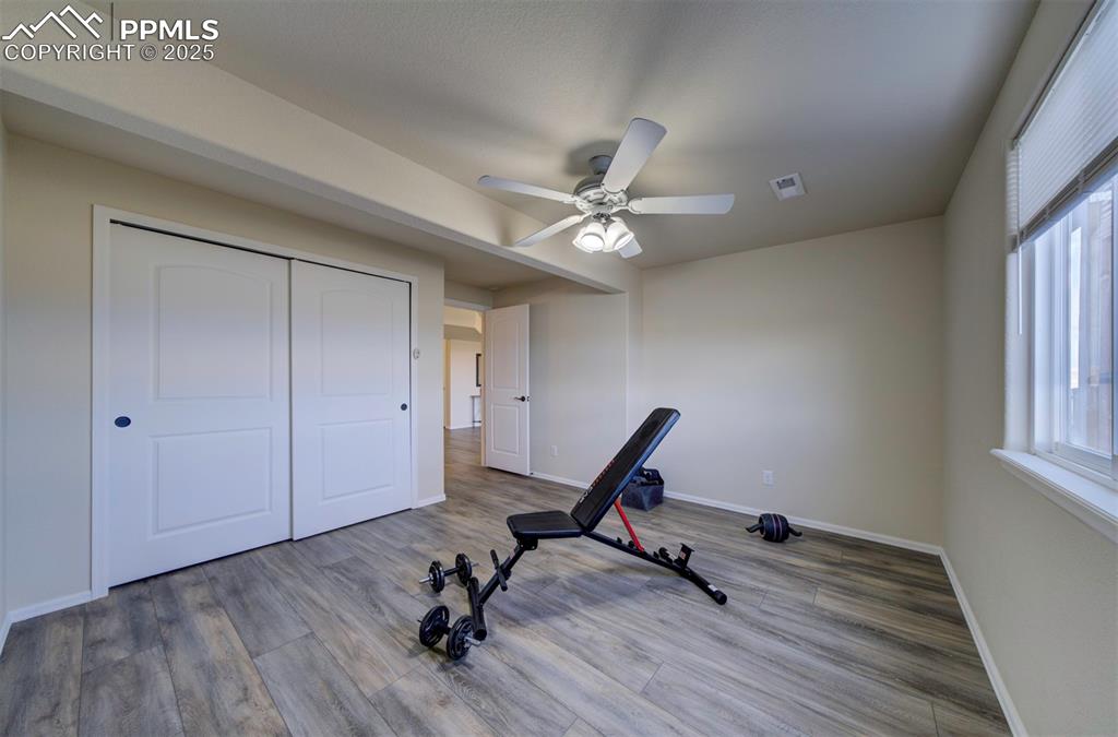 Image 32 of 45: Bedroom in basement currently used as a work out room, closet, ceiling fan,