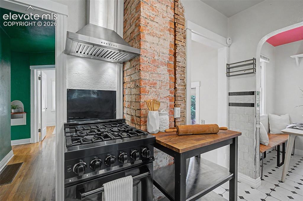 Image 16 of 37: Freestanding gas range with stainless steel hood, exposed brick column, woo