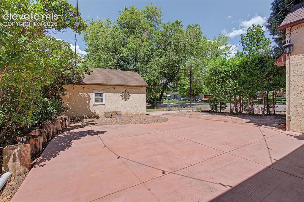 Image 31 of 37: Expansive concrete patio with an adjacent detached stucco shed, mature peri