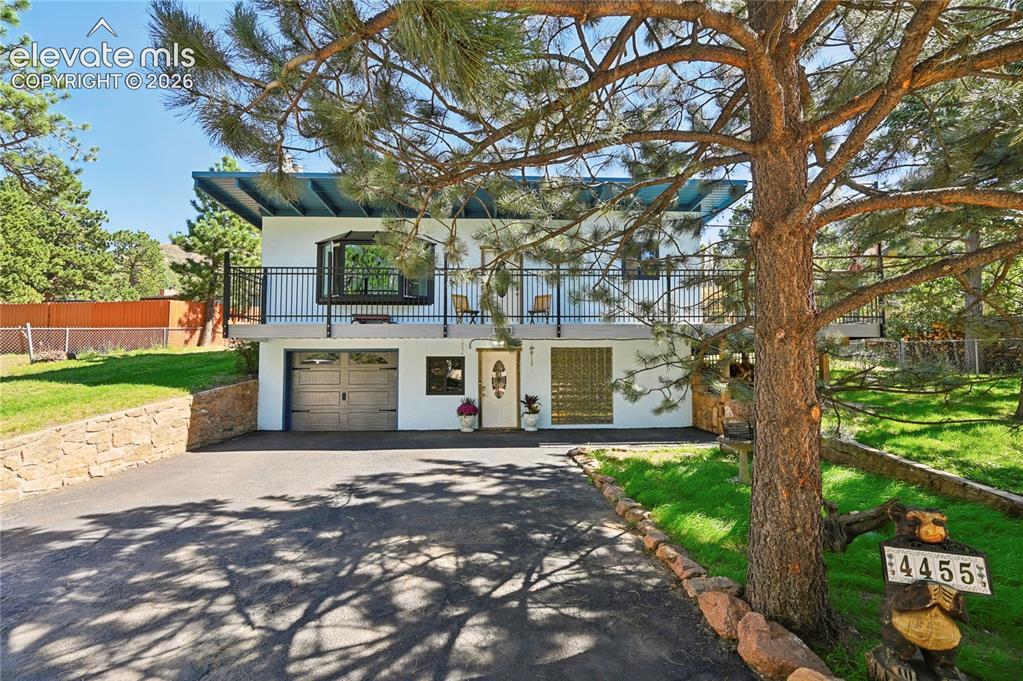 Caption: Split-level residence featuring a prominent covered balcony with black railings, an attached garage,