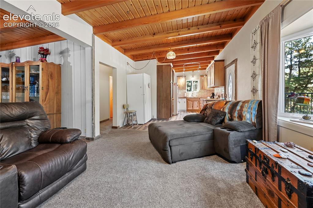Image 10 of 50: Vaulted wood-paneled ceiling with exposed beams, carpeted flooring, kitchen