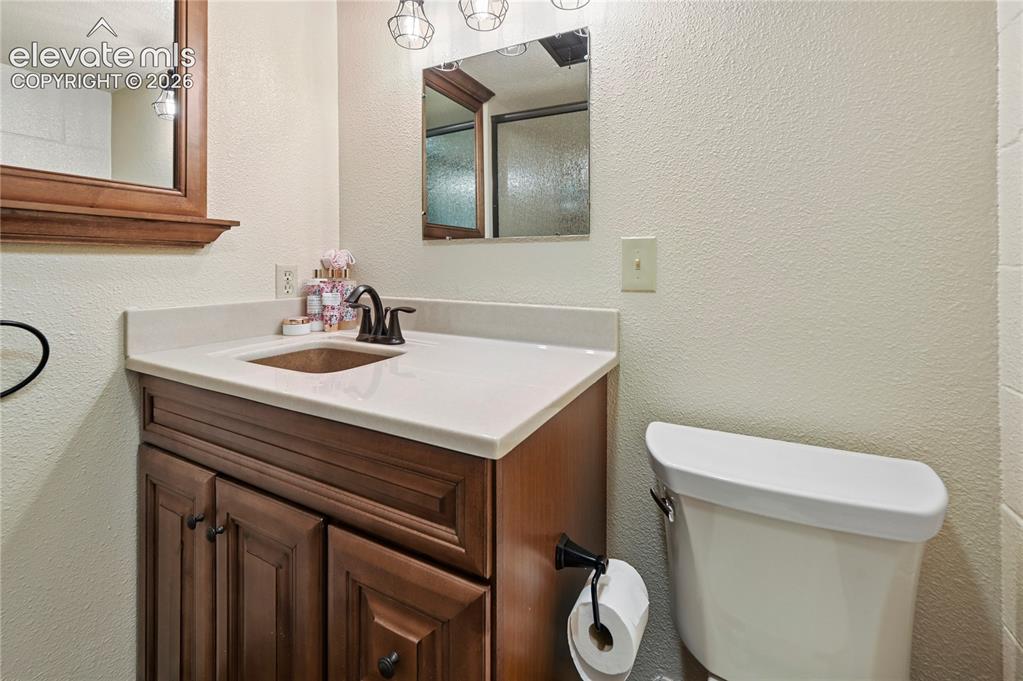Image 20 of 50: Wood-finish vanity with panel detailing, light-toned countertop, and bronze
