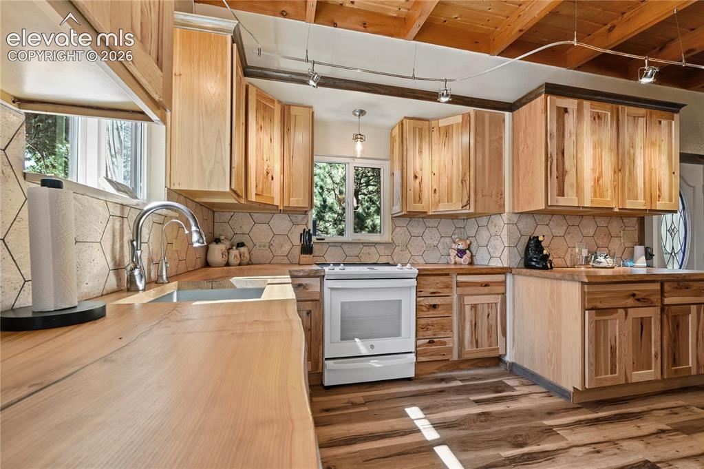 Image 3 of 50: Wood-finish flooring, wood cabinetry, hexagonal tile backsplash, window ove