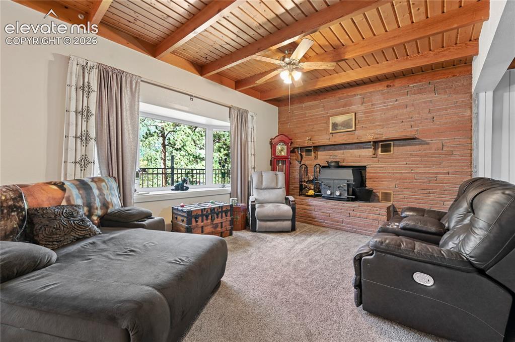 Image 8 of 50: Exposed wood beam ceiling, brick accent wall with fireplace, bay window, an