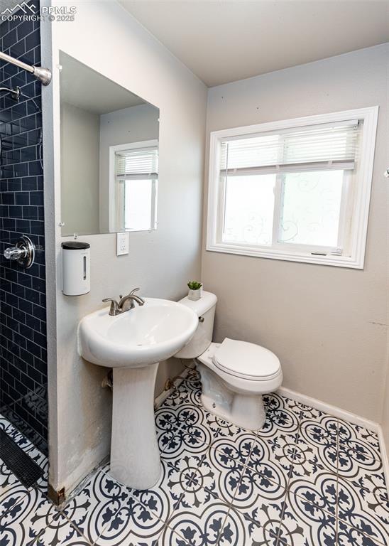 Image 18 of 25: Full bathroom with a tile shower, toilet, tile patterned flooring, and base