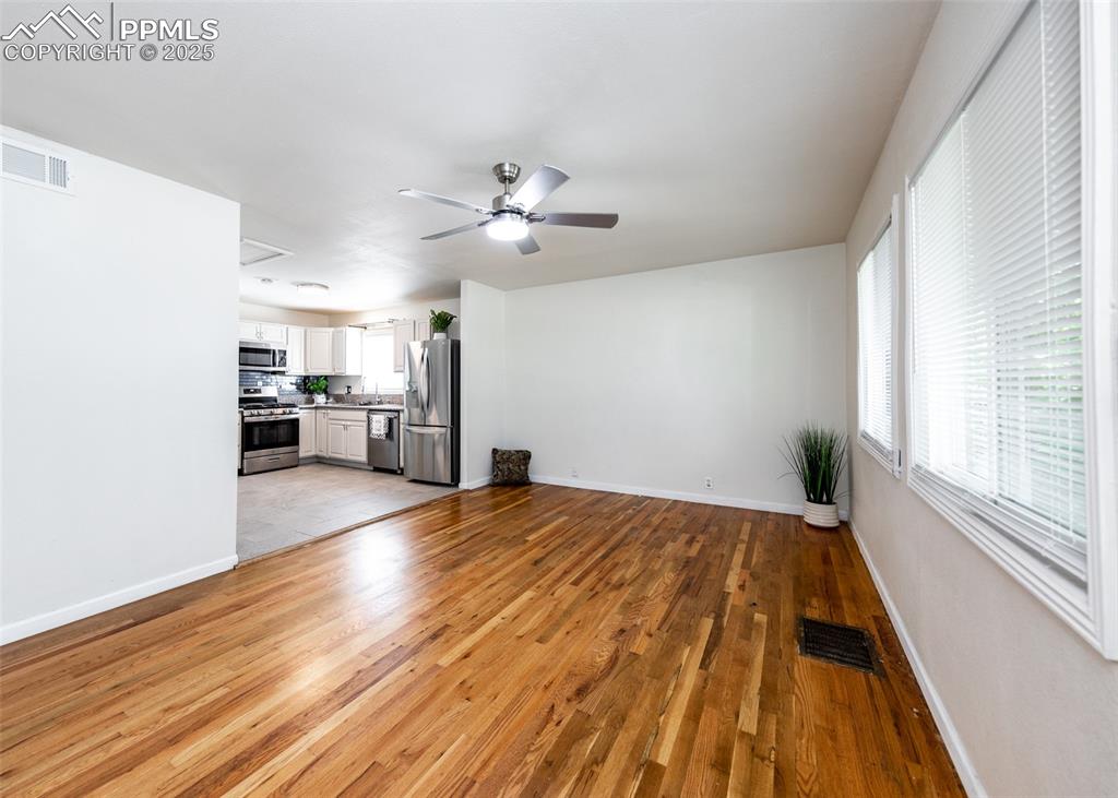 Image 6 of 25: Unfurnished living room with a ceiling fan, light wood-type flooring, baseb
