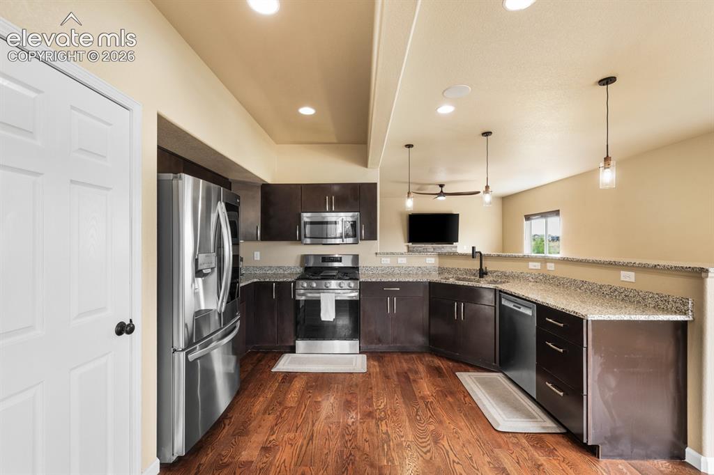 Image 14 of 50: Kitchen featuring dark wood cabinetry, stainless steel appliances, speckled
