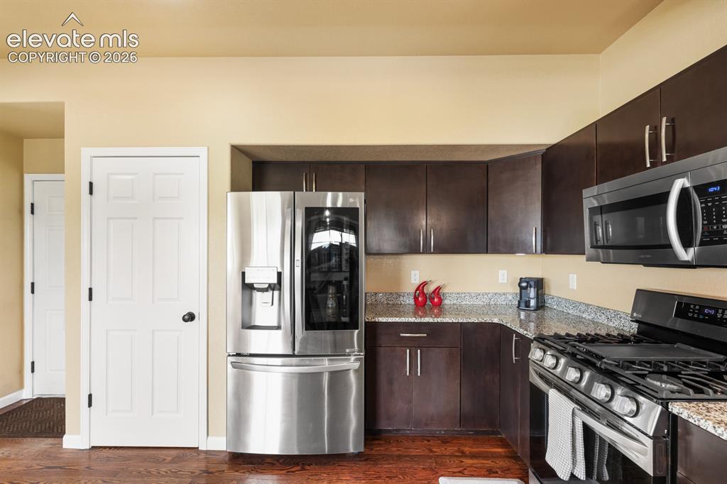 Image 16 of 50: Kitchen featuring dark wood-finish cabinetry, granite countertops, and stai