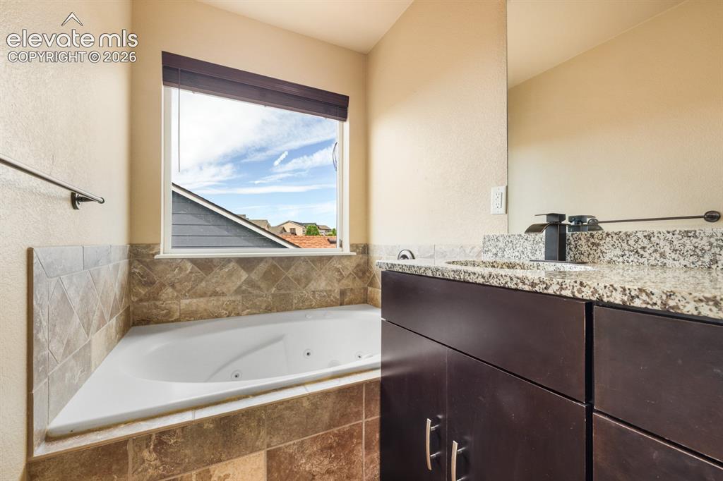 Image 21 of 50: Corner soaking tub with textured tile surround, wood-finish vanity with a s