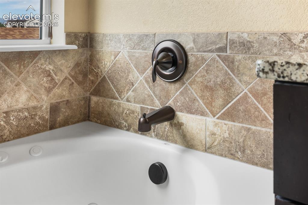 Image 22 of 50: White soaking tub featuring a bronze-finish faucet, tiled surround, and tex