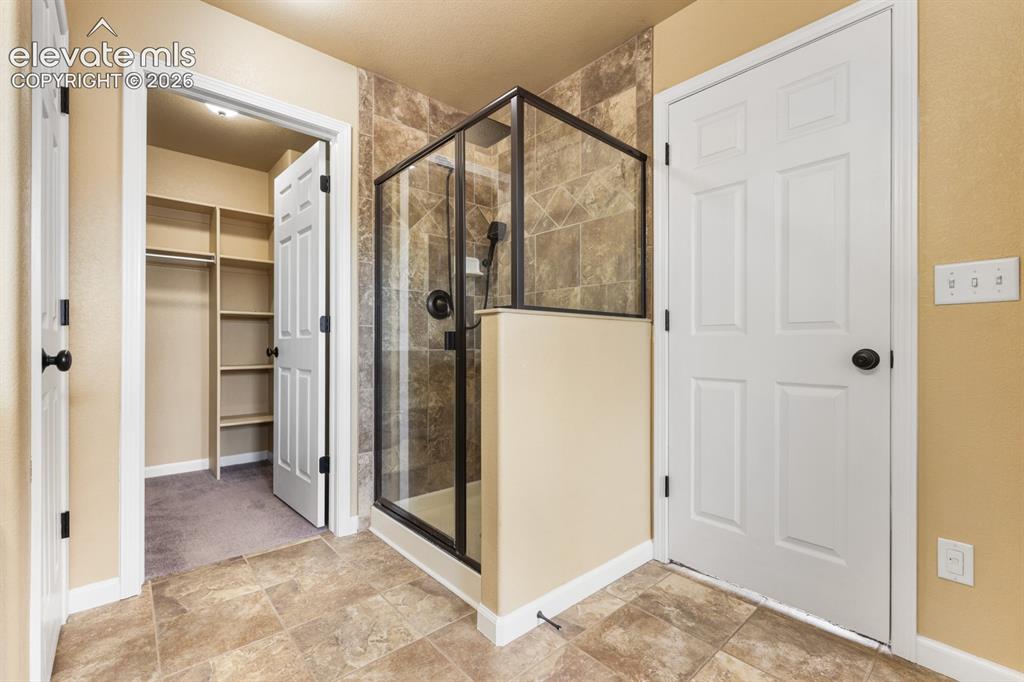 Image 23 of 50: Walk-in shower with glass enclosure and dark trim, tile flooring, and integ