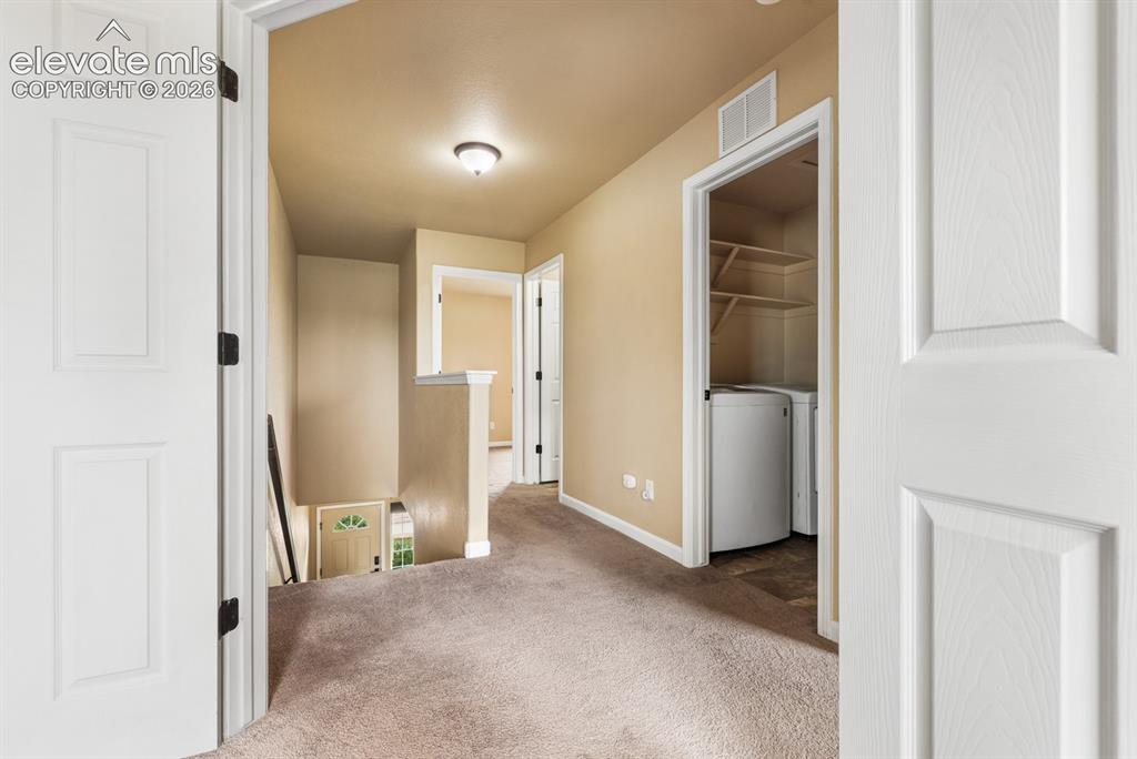 Image 26 of 50: Carpeted hallway with a built-in laundry area featuring a washer and dryer,
