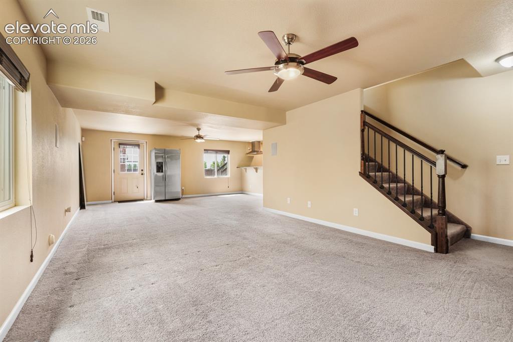 Image 34 of 50: Carpeted open-concept room with a ceiling fan, a window with a roller shade