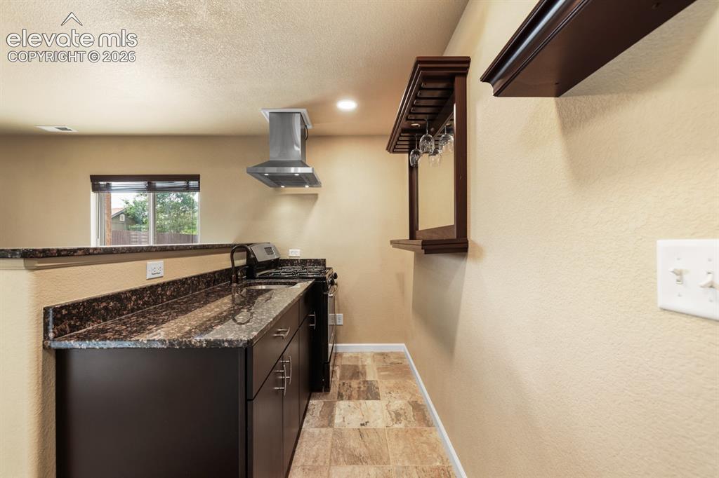 Image 38 of 50: Compact kitchen area featuring dark wood-finish cabinetry, a black faucet,