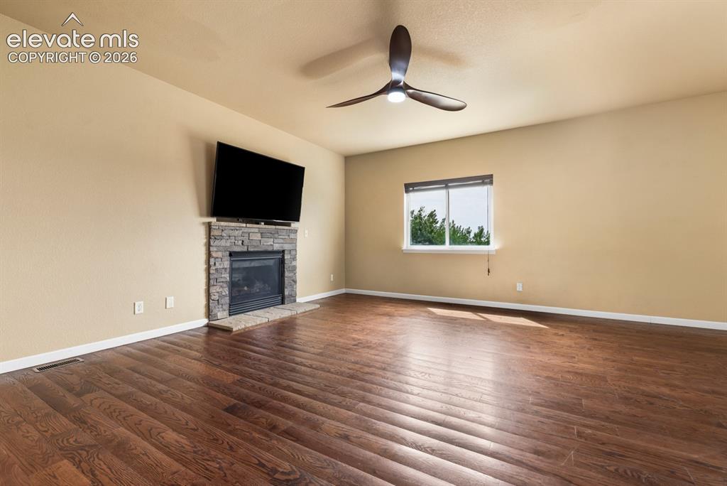 Image 6 of 50: Spacious room featuring wood-finish flooring, a stone-clad fireplace with a