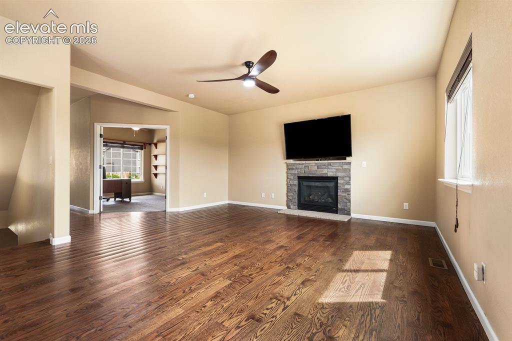 Image 8 of 50: Open-concept living area featuring wood-finish flooring, a stone-clad firep