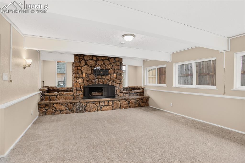 Image 20 of 37: Lower level living space with stone fireplace and abundant natural light.