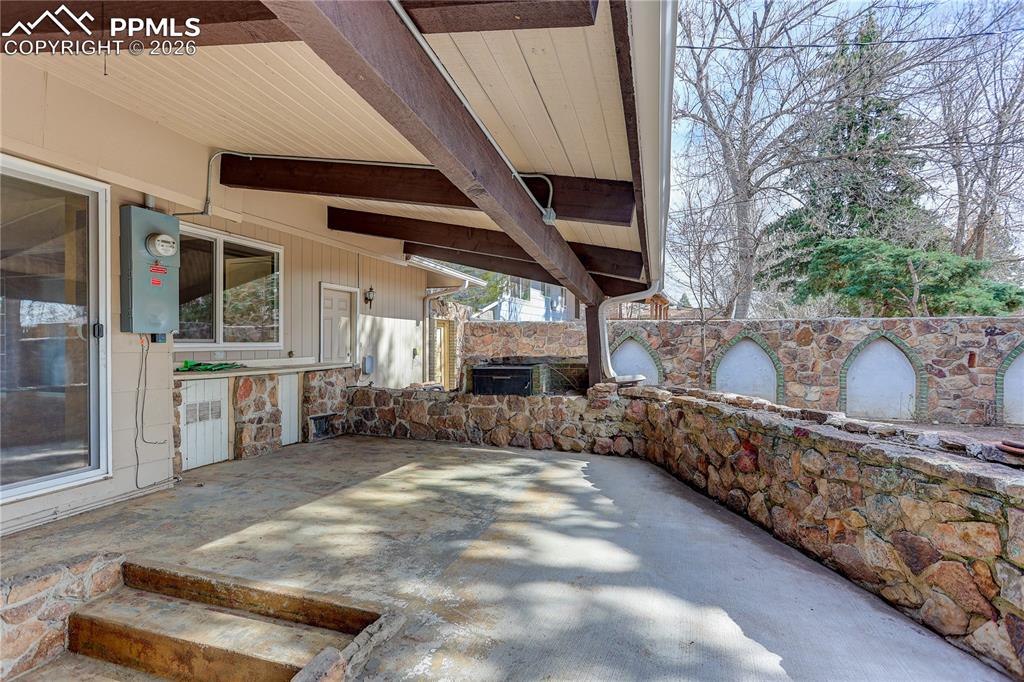 Image 34 of 37: Covered patio space with stonework and outdoor grill.