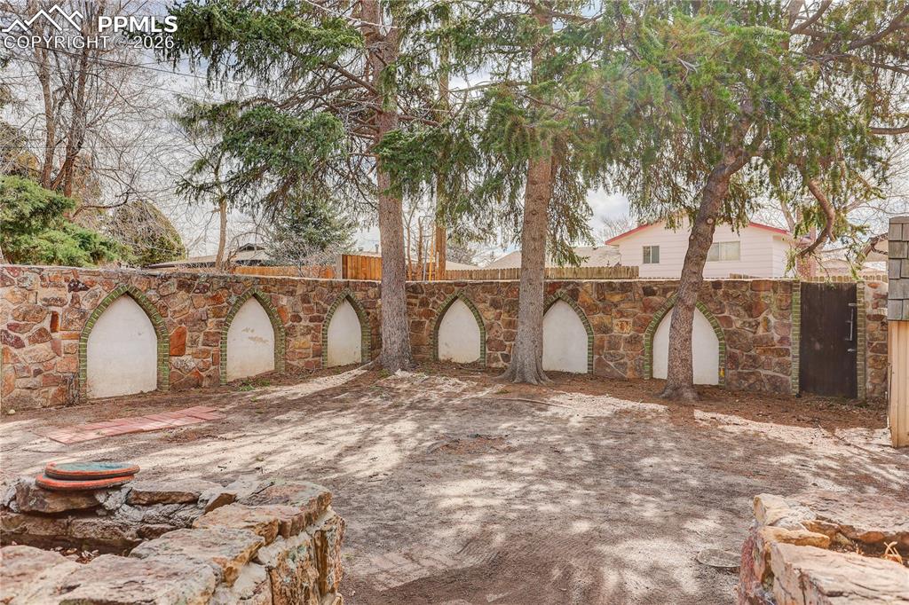 Image 37 of 37: Backyard with mature trees and distinctive stone privacy wall.