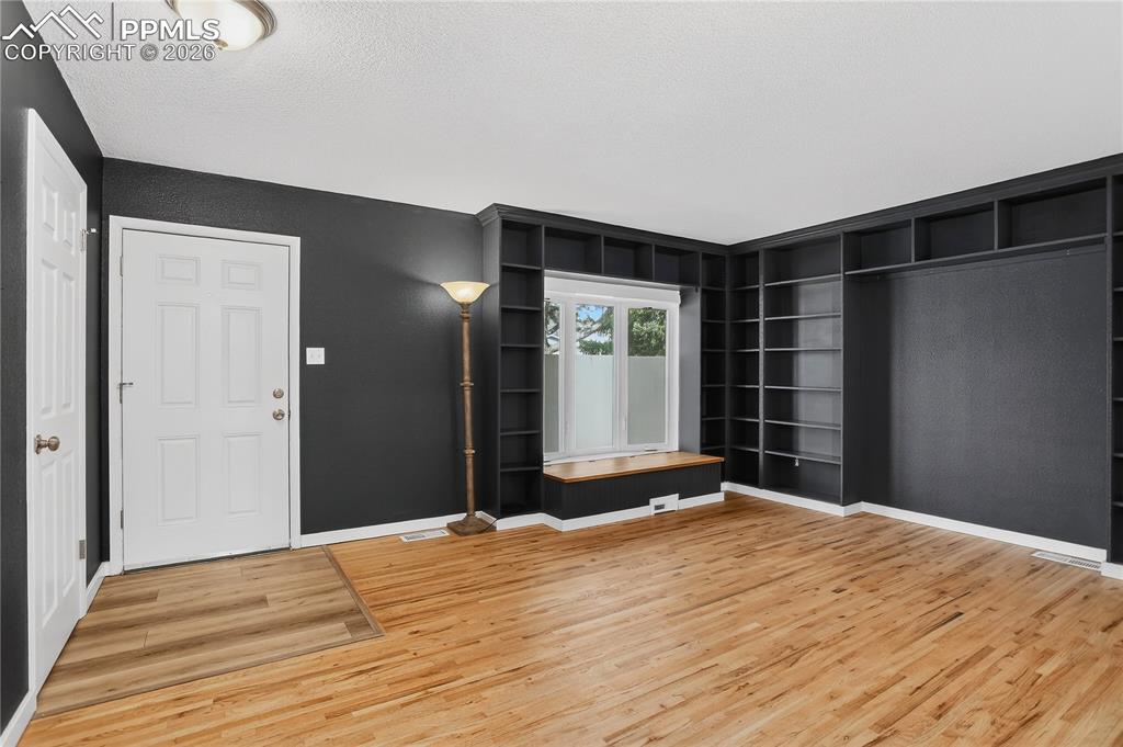 Image 7 of 37: Living room with hardwood flooring, built-in shelving, and bay window with 