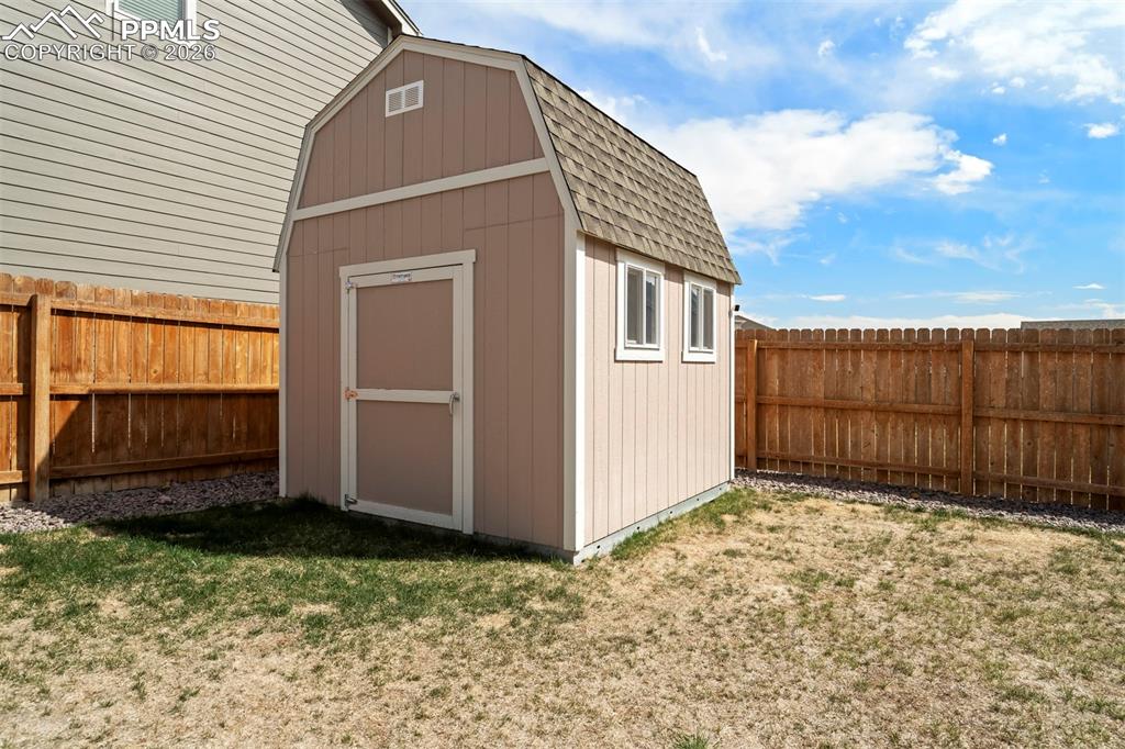 Image 41 of 46: Barn-style shed featuring a shingle roof, two windows, and a fenced yard