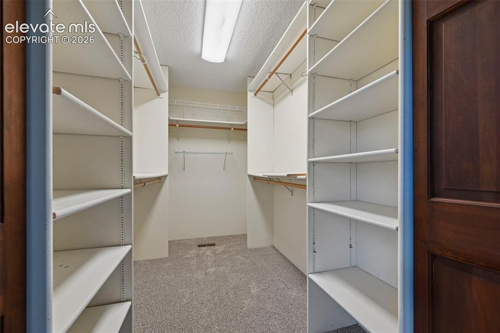Image 23 of 50: Walk-in closet featuring adjustable shelving, multiple hanging rods, and ca