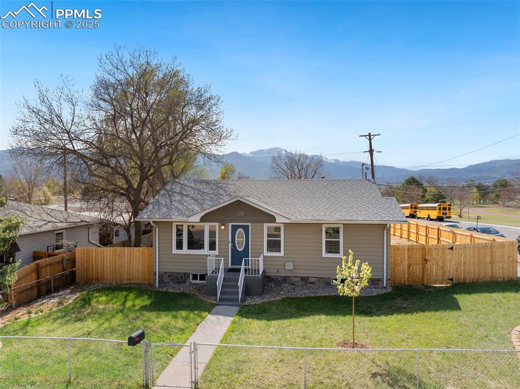 Caption: Bungalow with a fenced backyard, a front lawn, roof with shingles, and a mountain view
