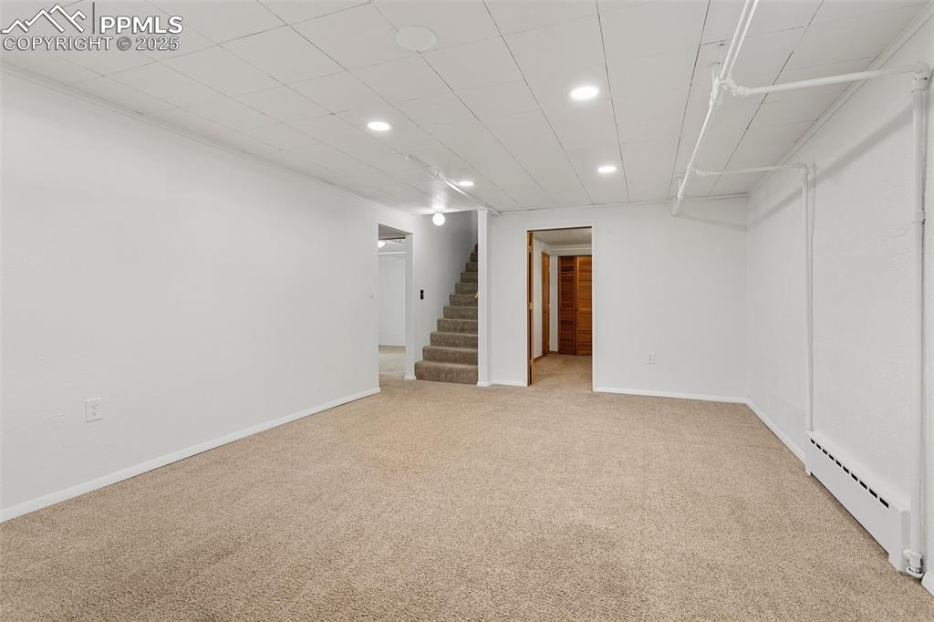 Image 26 of 37: Finished basement with stairs, a baseboard heating unit, baseboards, carpet
