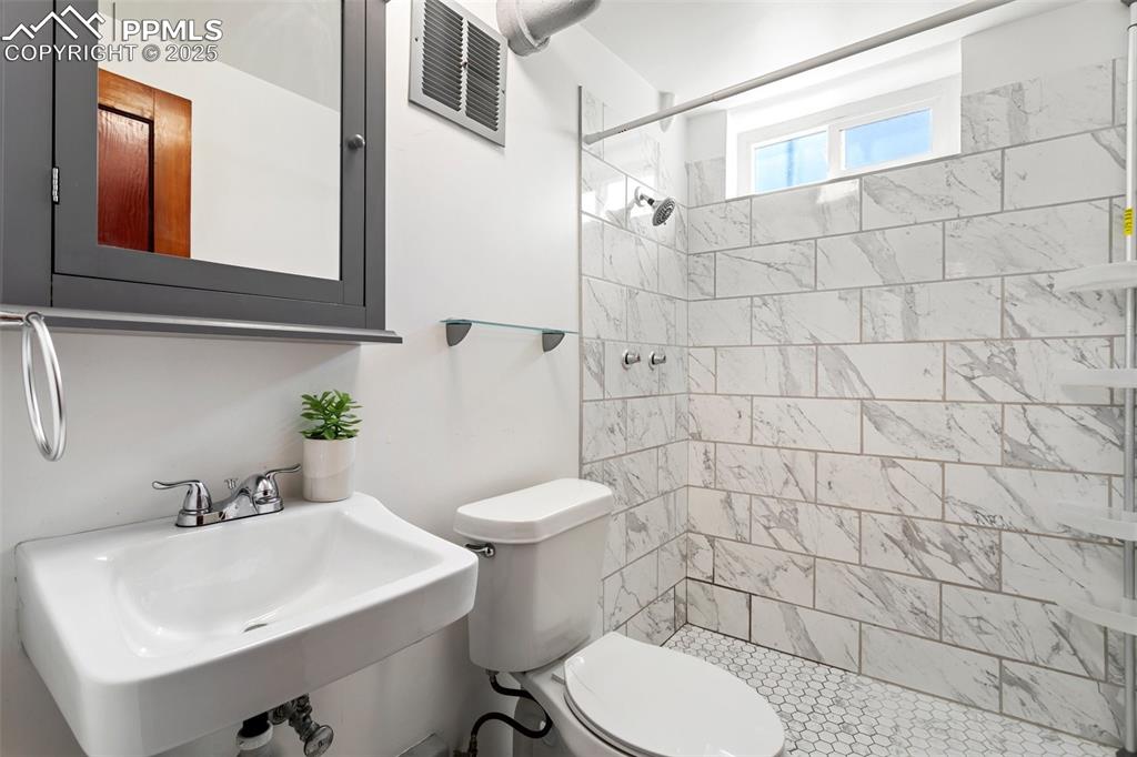 Image 29 of 37: Basement bathroom with a shower stall, toilet, a sink, and visible vents